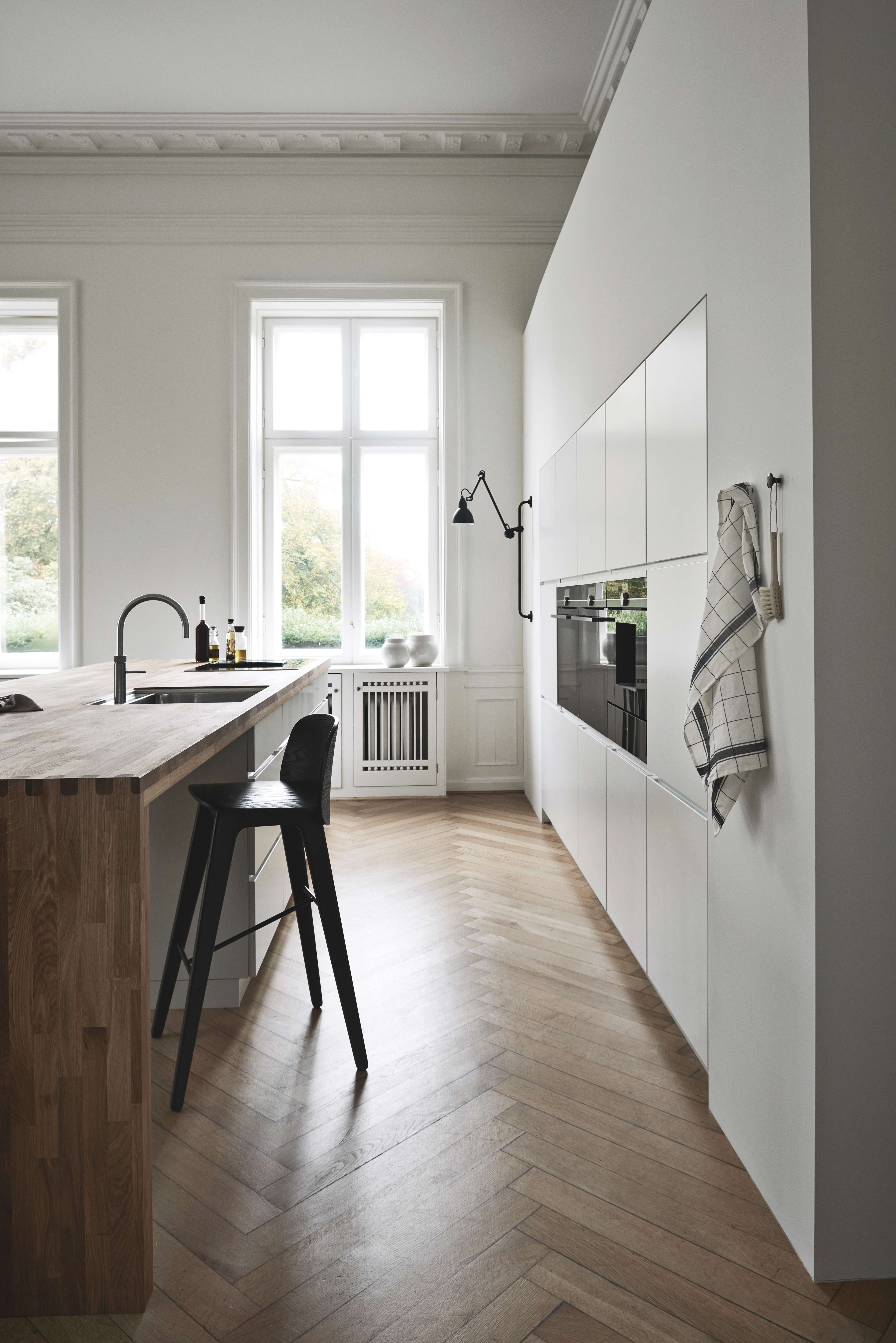 MANO witte keuken met strakke kasten, minimalistisch design, inbouwapparatuur en een houten aanrechtblad, waardoor een strakke en moderne culinaire ruimte ontstaat.