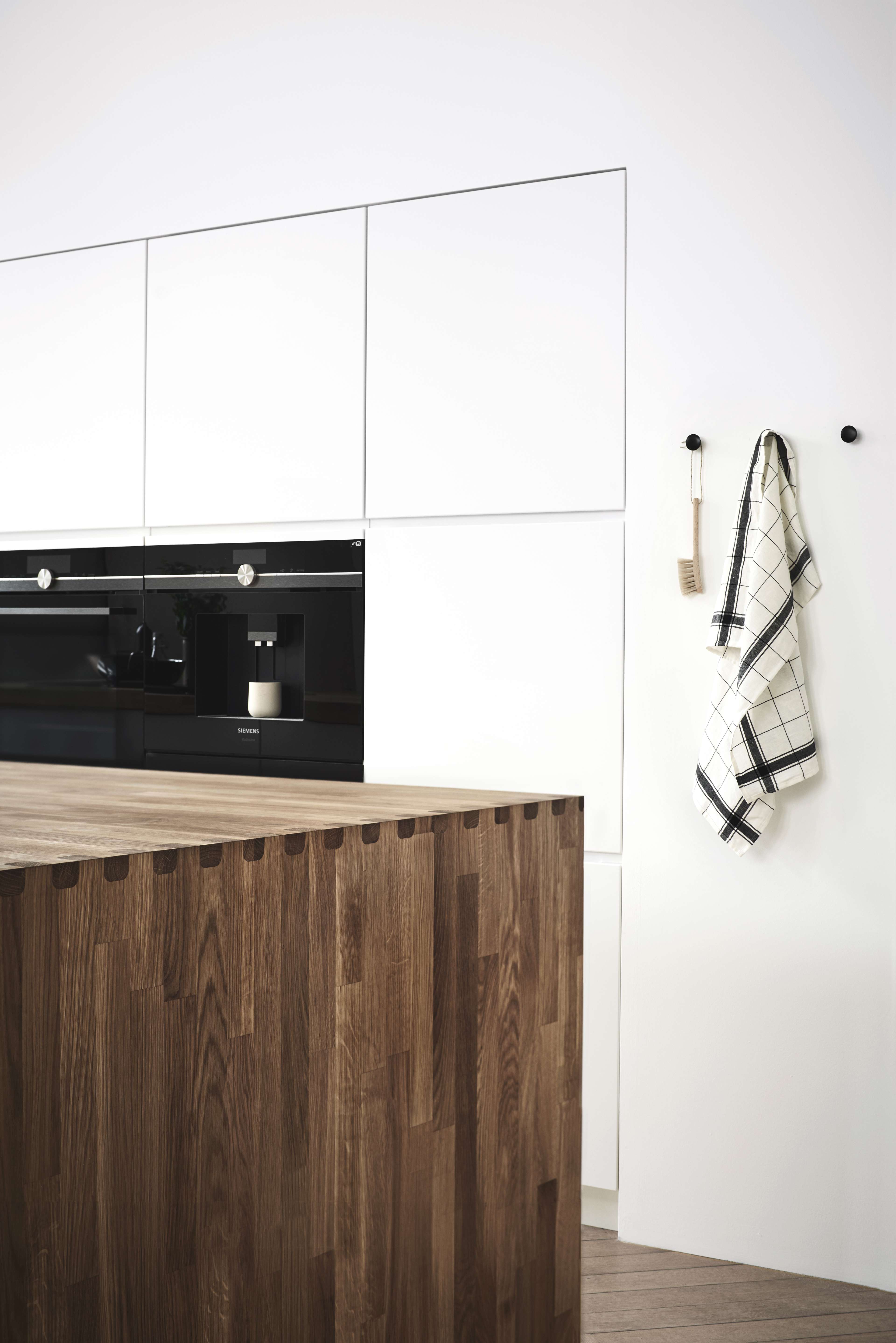 MANO vitt kök med minimalistisk design, med snygga handtagslösa skåp och en rik träö, vilket skapar en modern och elegant matlagningsplats.