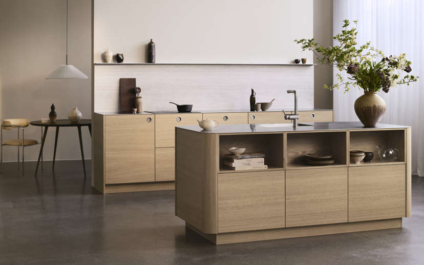 VEDA lyst egetræskøkken med minimalistisk design, med glat skab og en moderne ø, der skaber et varmt og organiseret madlavningsrum.