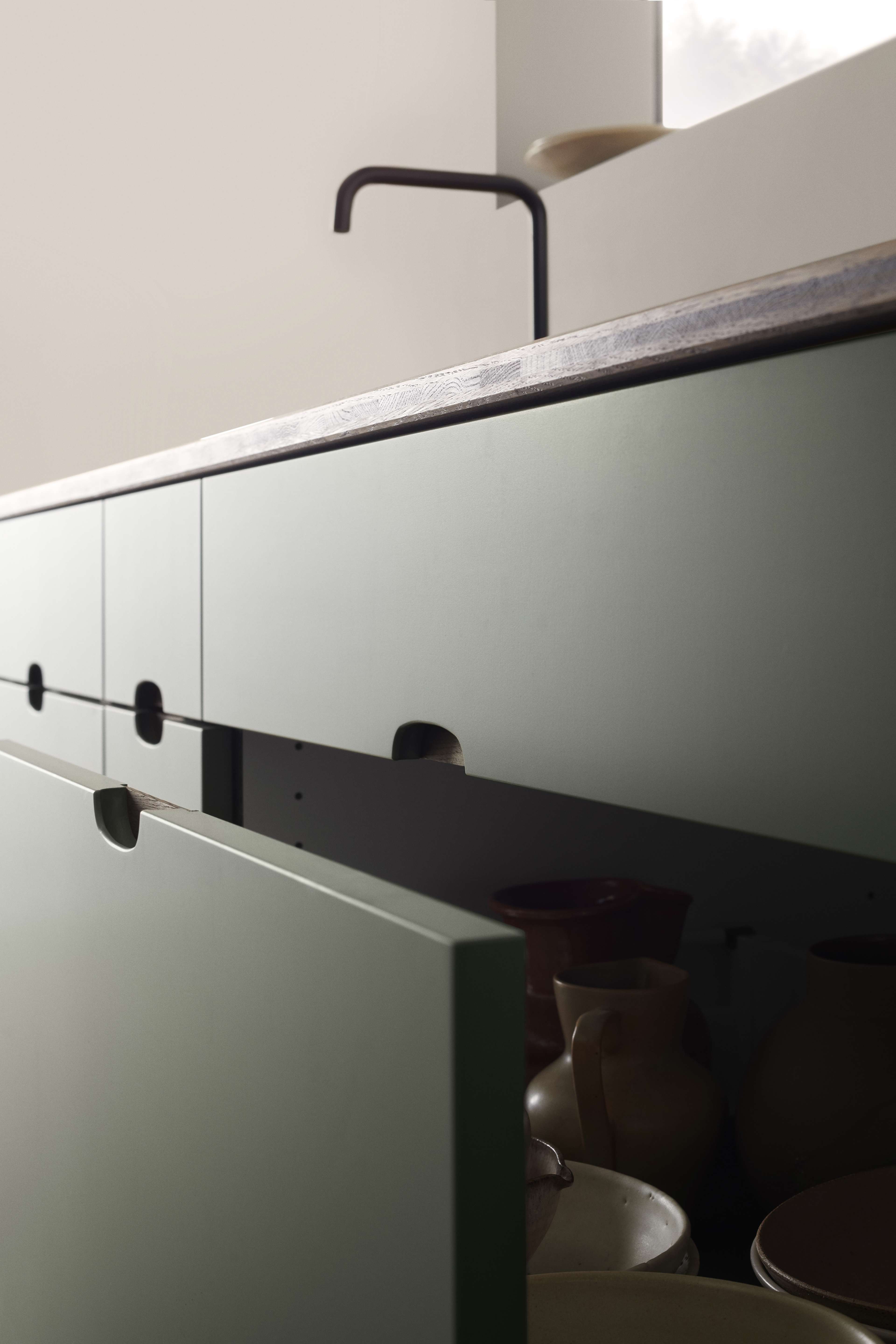 OMBRA grönt köksskåp med elegant, sömlös design utan handtag, som erbjuder en modern estetik och gott om förvaringsutrymme under en mörk bänkskiva.