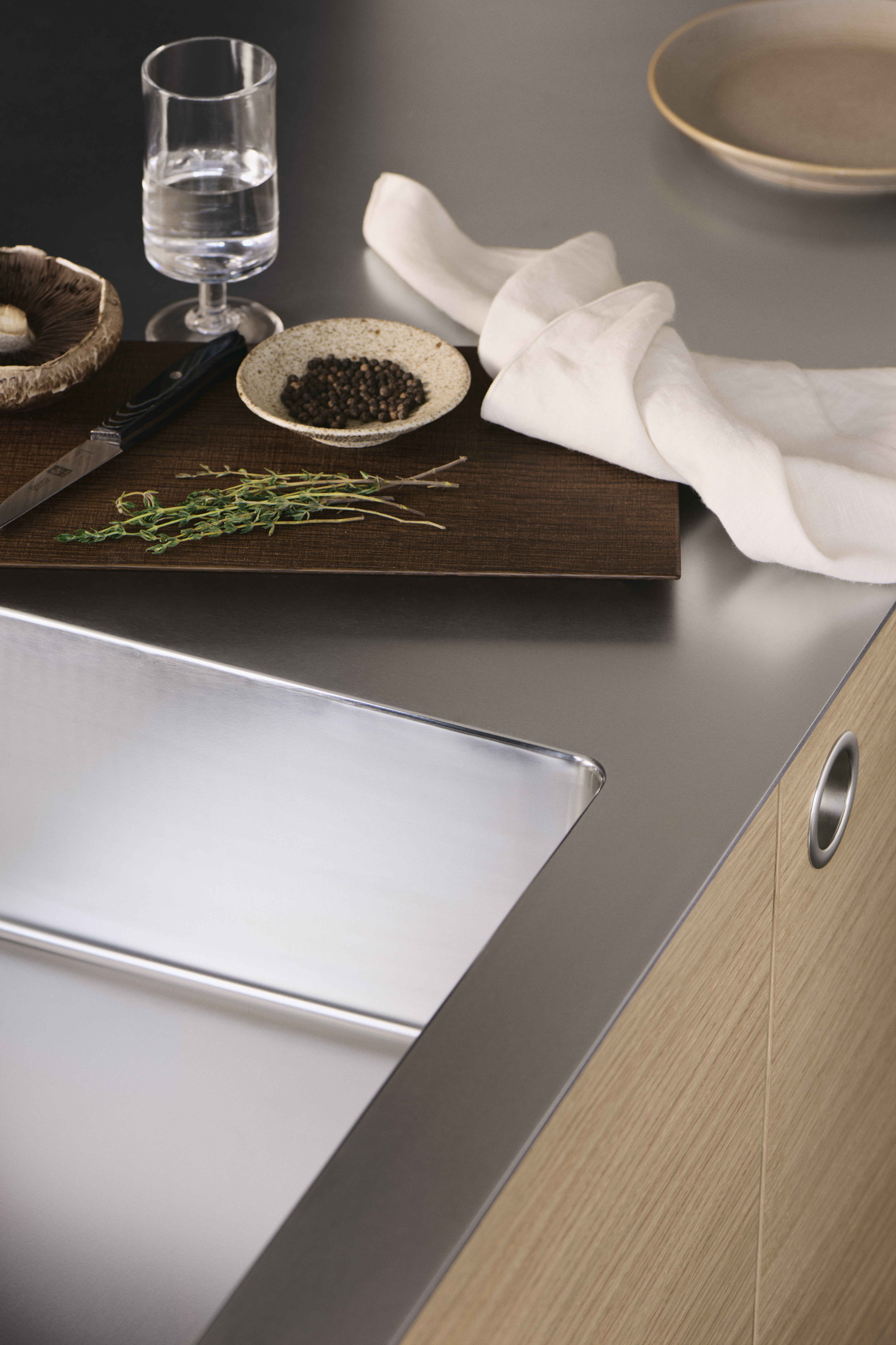 Cocina VEDA de roble claro con elegante encimera de acero inoxidable y tiradores integrados, que combina un diseño contemporáneo con una elegancia práctica.