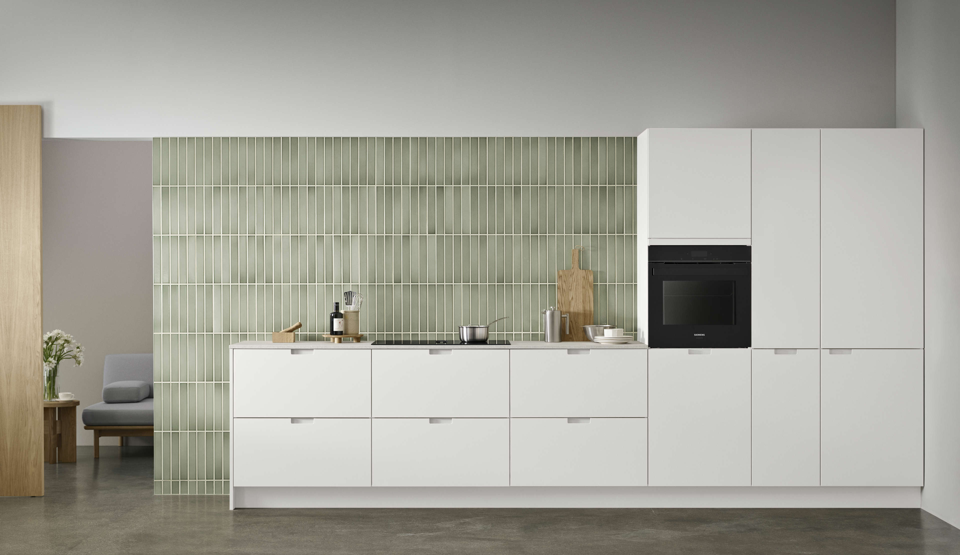 EVENTO white kitchen cabinets with sleek, minimalist design and integrated handles against a contemporary light green tiled backsplash.