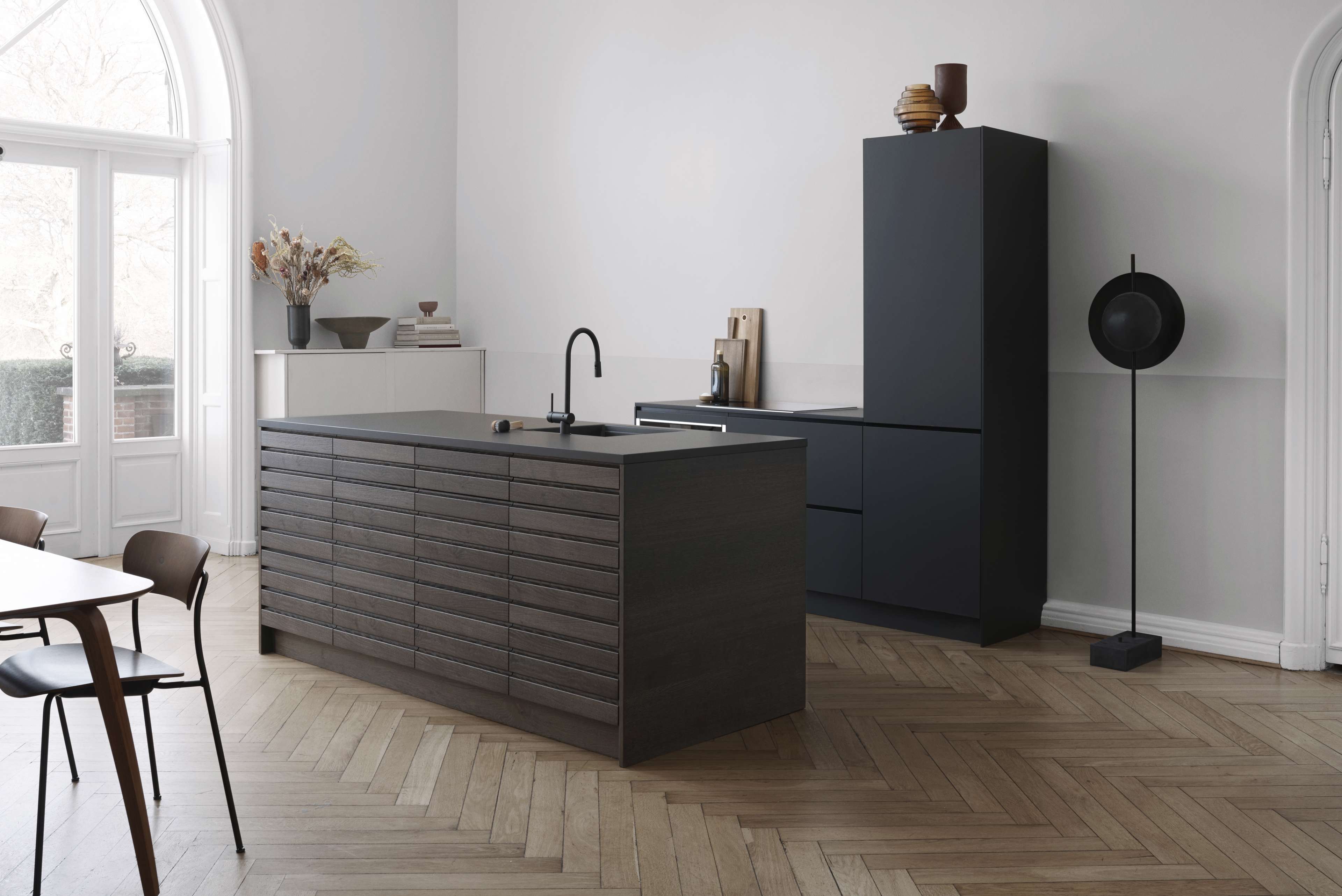 Cuisine CIMA en chêne foncé au design minimaliste avec des armoires élégantes et un îlot moderne, posée sur un plancher en bois à chevrons pour une élégance raffinée.
