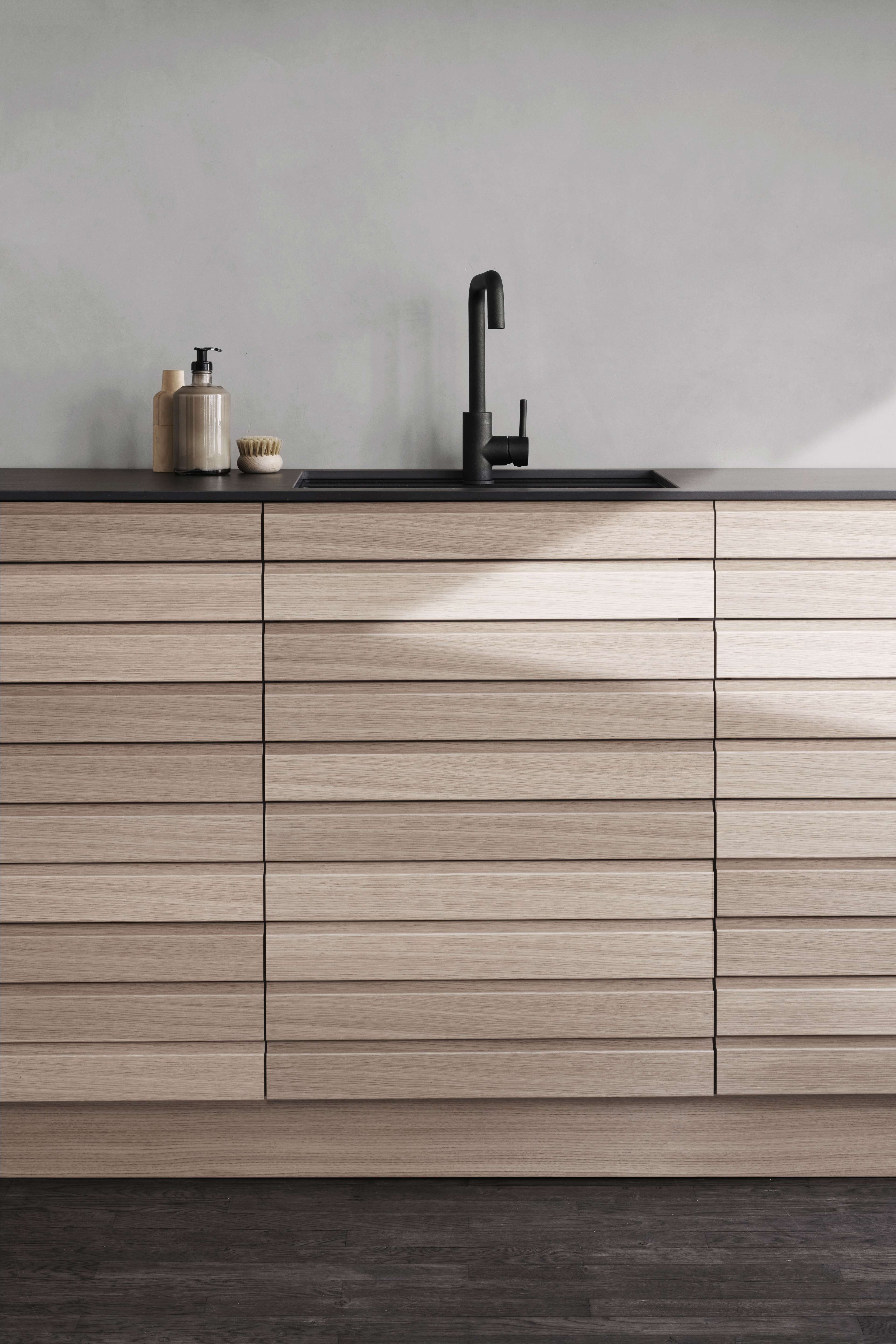 CIMA köksskåp i ljus ek med elegant horisontellt ådring, minimalistisk svart bänkskiva och modern blandare, som förstärker nordisk elegans.