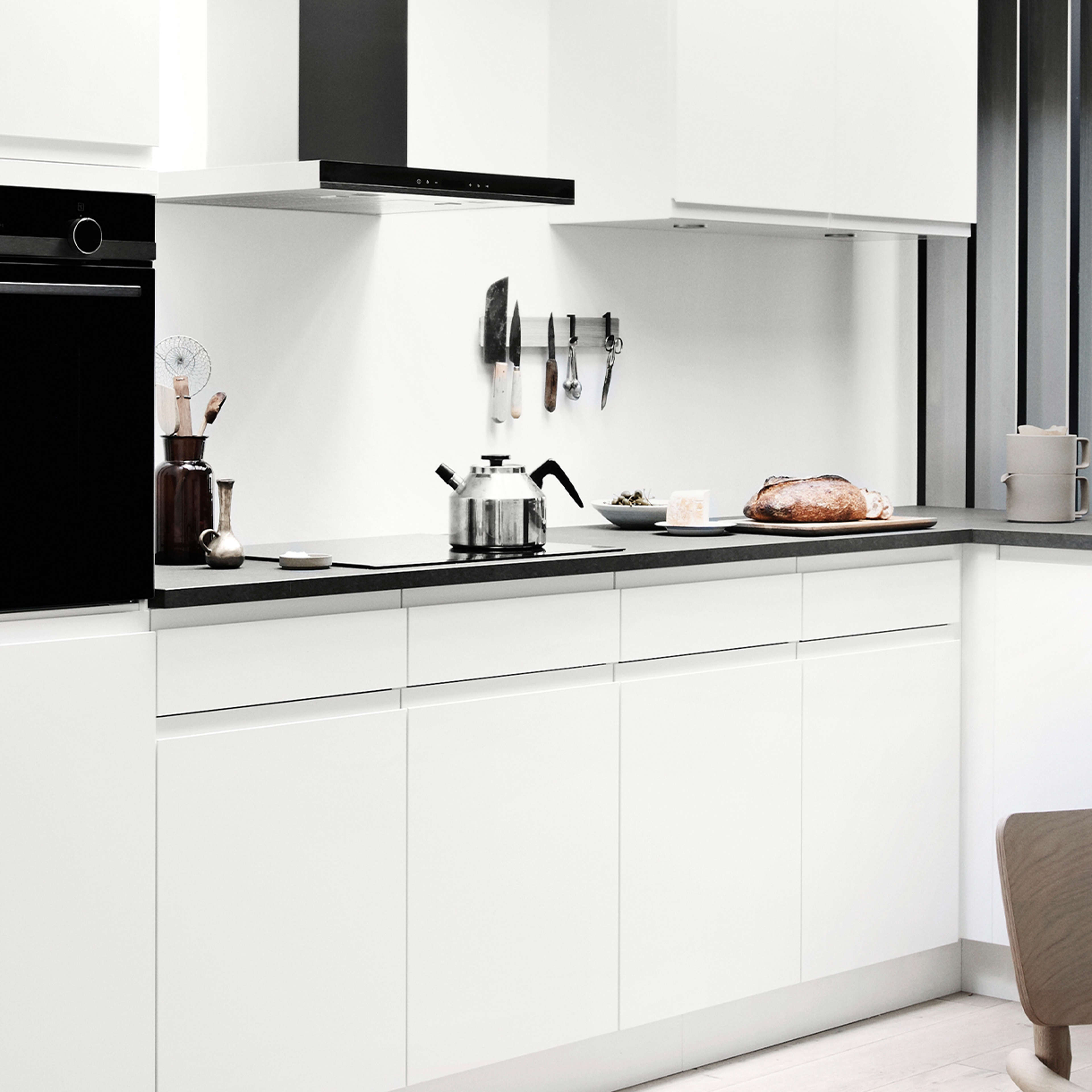 NOLIAM hvidt køkken med slanke minimalistiske skabe og moderne sorte accenter, der kombinerer moderne design med et rummeligt og organiseret layout.
