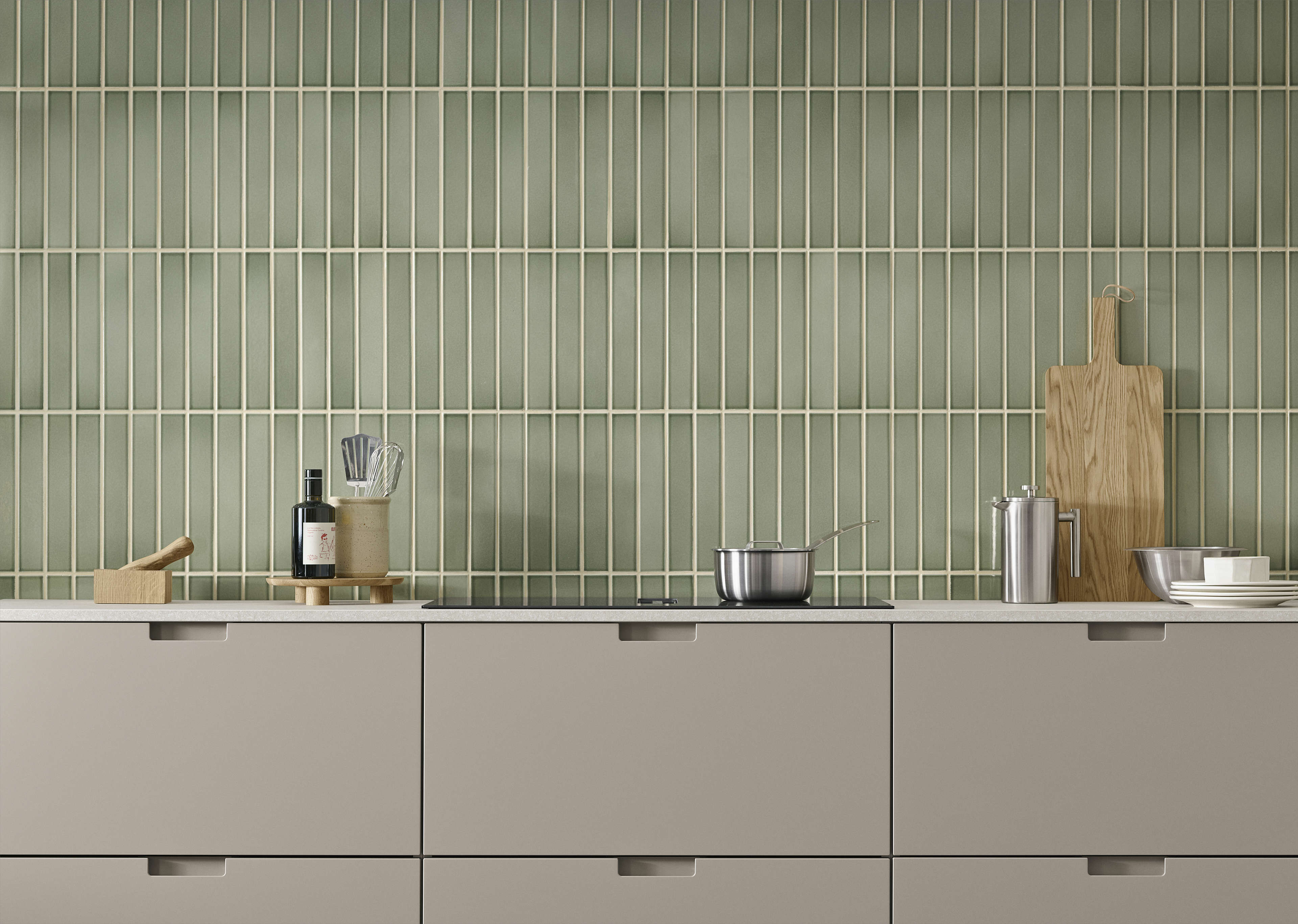 EVENTO arizona beige kjøkkenskap med elegante håndtak mot en grønn flislagt vegg, og tilbyr et moderne og minimalistisk kulinarisk rom.